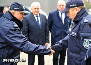 Zastępca Komendanta Wojewódzkiego Policji wita się z policjantem, a w tle inne osoby.