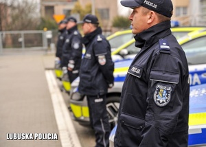 Policjanci stojący w rzędzie przed radiowozami.
