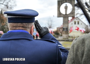 Policjant oddaje honor przed pomnikiem.