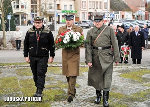 Żołnierz i pozostałe osoby składają kwiaty przed pomnikiem.