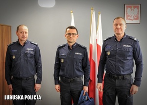 Policjanci pozują do zdjęcia na tle flag Polski.