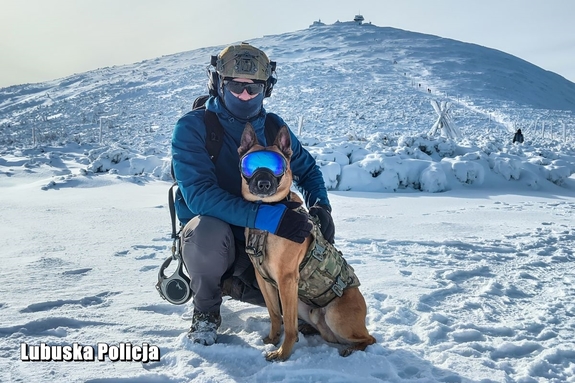 mężczyzna z policyjnym psem stoją przed szczytem góry