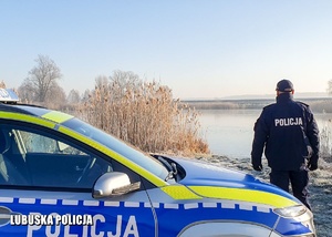 Policjant stojący przy radiowozie sprawdza zamarznięte jezioro.