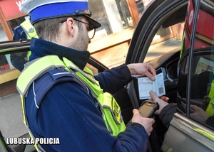 Policjant drogówki sprawdza dokumenty od pojazdu.