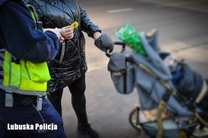 Policjant drogówki wręcza element odblaskowy kobiecie z wózkiem dziecięcym.