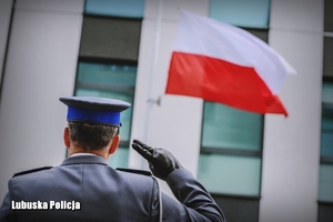 Policjant oddaje honor na tle flagi Polski.