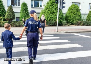 Policjantka podczas przeprowadzania dziecka przez przejście dla pieszych.