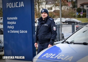 Umundurowany policjant stojący przy radiowozie.