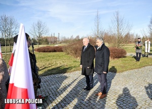 Wojewoda Lubuski wraz z mężczyzną oddają honory przed pomnikiem.