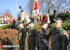 Poczet sztandarowy żołnierzy przed pomnikiem.
