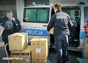 Policjanci pakują kartony z prezentami do radiowozu.