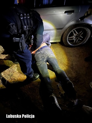 Zatrzymany leżący na ziemi kajdankowany przez policjanta