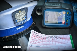 Blankiet mandatu karnego, policyjna czapka i urządzenie do pomiaru prędkości jadących pojazdów.