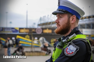 policjant stoi przy stadionie żużlowym i obserwuje zachowanie kibiców