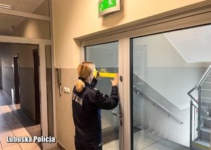 Policjantka nakleja taśmę na drzwiach w budynku komendy Policji.
