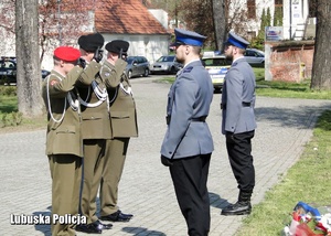 Żołnierze oddają honory przed pomnikiem.