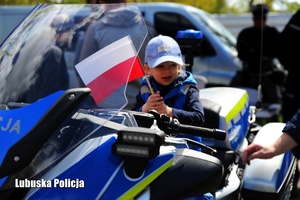 Chłopiec na policyjnym motocyklu trzymający w dłoni flagę Polski.