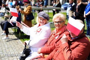 Starsze kobiety siedzące na ławce i trzymające w dłoniach flagę Polski.