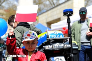 Chłopiec trzymający flagę Polski, a za nim policyjny motocykl.