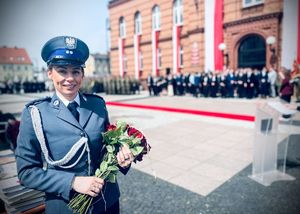Policjantka z bukietem kwiatów na tle szkoły.