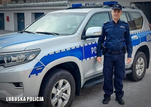 Umundurowany policjant stojący przy radiowozie.