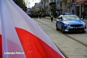 Flaga Polski, a w tle jadący radiowóz.