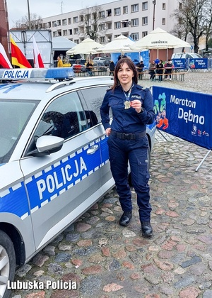 Policjantka stojąca przy radiowozie podczas zawodów biegowych.