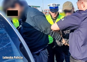 Zatrzymany mężczyzna ma zapinane kajdanki na ręce przez policjantów.