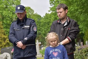 Policjant oraz pozostałe osoby na cmentarzu.