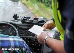 Policjant drogówki kontroluje dokumenty kierowcy autokaru.