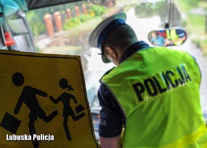 Tabliczka oznaczająca przewóz dzieci, a w tle policjant przeprowadzający kontrolę drogową.