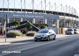 Policyjny radiowóz na tle stadionu żużlowego.