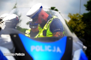Motocykl policyjny, a za nim policjant ruchu drogowego.