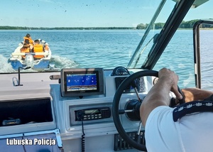 Policjant kierujący motorówką, a w tle inna łódź na jeziorze.