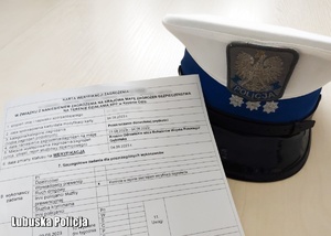 Karta weryfikacji zgłoszenia obok czapki policjanta ruchu drogowego.