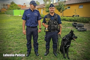 Policjanci stojący obok psa służbowego.