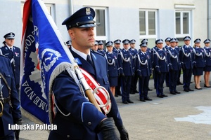 Poczet sztandarowy Policji, a w tle policjanci stojący w szeregu.