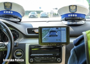 Czapki policjantów ruchu drogowego w radiowozie i wyświetlacz policyjnego videorejestratora.