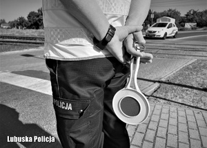 Czarno białe zdjęcie - policjant stojący przy przejeździe kolejowym.