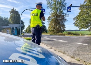 Policyjny radiowóz, a przed nim policjant kontrolujący prędkość pojazdów.