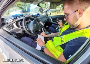 Policjant drogówki wypisuje mandat karny siedząc w radiowozie.