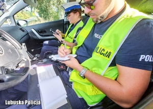 Policjanci drogówki podczas przeprowadzania czynności legitymowania i wypisania mandatu w radiowozie.