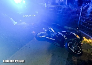 Przewrócony motocykl przy policyjnym radiowozie.