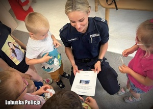 Policjantka w otoczeniu dzieci otrzymuje laurkę.