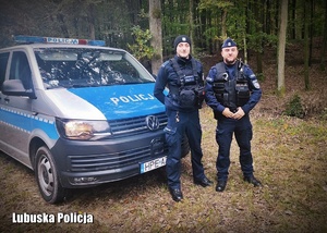 Policjanci stojący przy radiowozie w lesie.