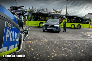 policyjny motocykli i policjant kontrolujący auto w tle