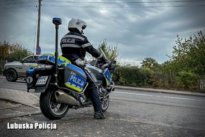 Policjant na motocyklu stoi przy drodze.