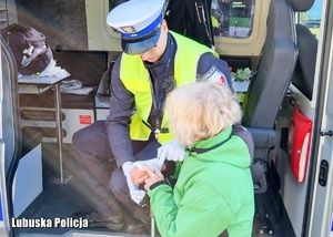 Policjant drogówki opatrujący rękę starszej kobiecie.