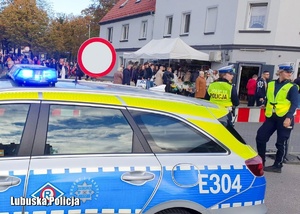 Policyjny radiowóz, a za nim policjantki drogówki podczas dnia Wszystkich Świętych.