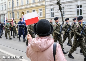 Kobieta mach flagą Polski w kierunku uczestników przemarszu.